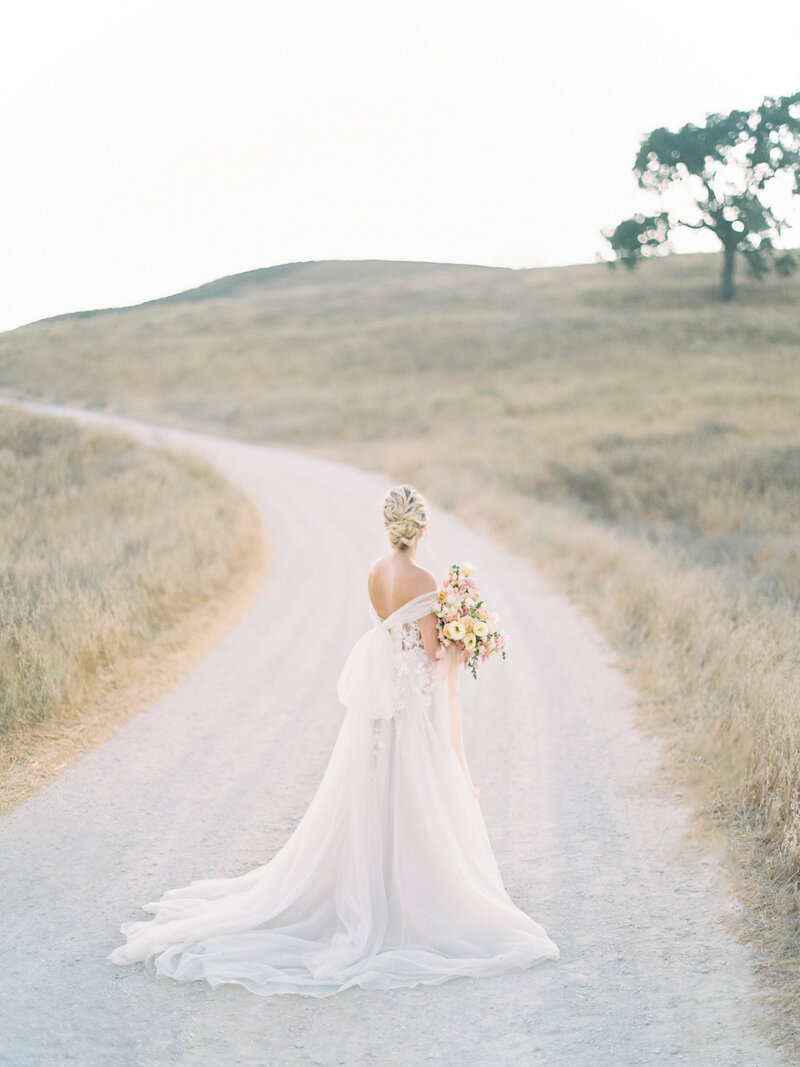 Bride holding flowers while standing on gravel road on contact Arielle Peters Photography page