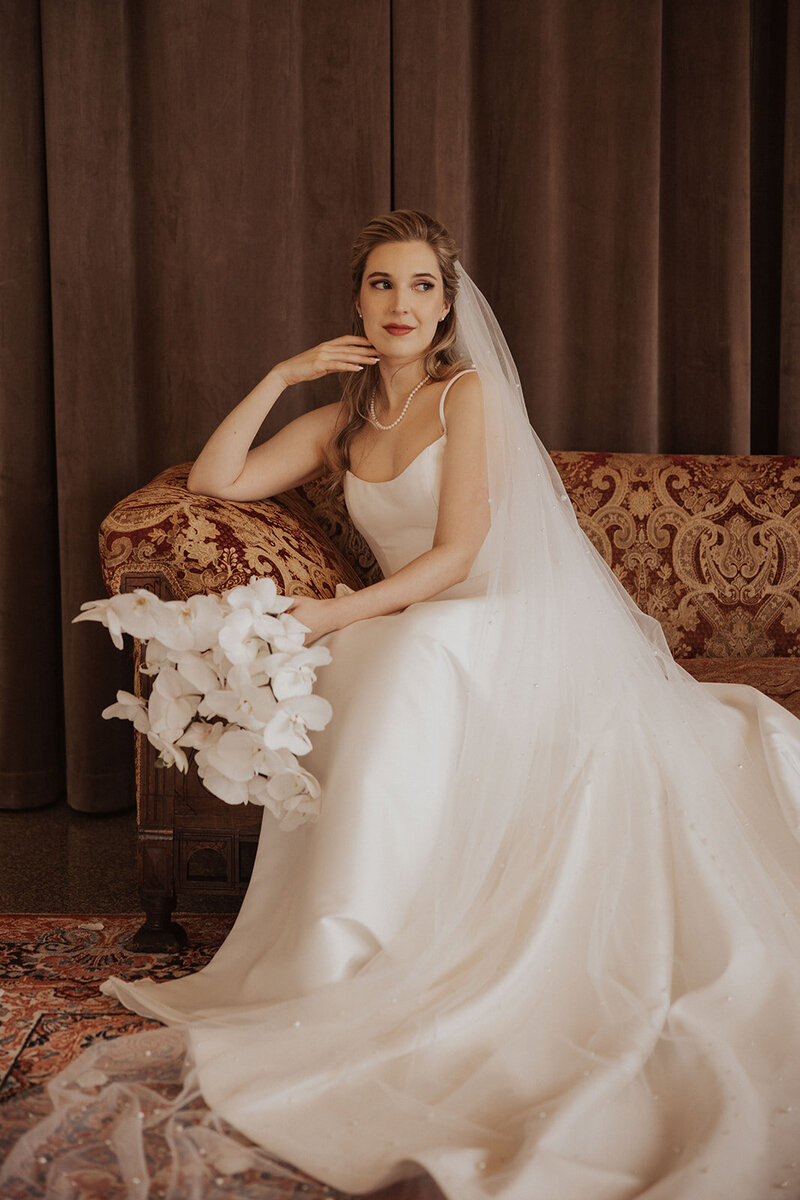 An elegant bride seated with a bouquet of white orchids, in a gown with a classic silhouette.