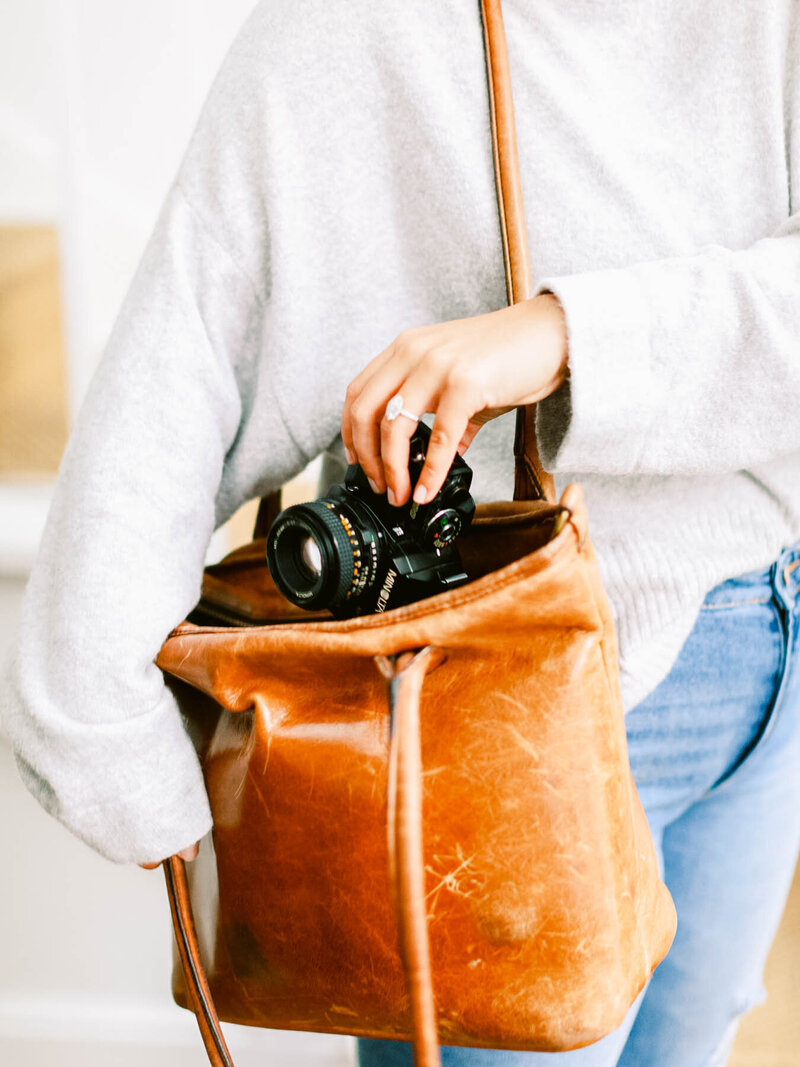women with leather bag on shoulder placing camera in bag
