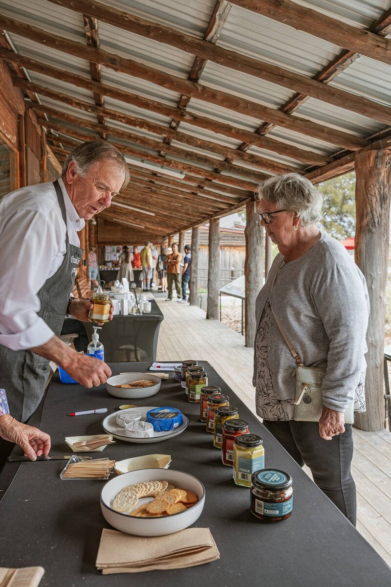 Local stallholder sharing Franklin Road Preserves samples with an attendee at a community event photographed by event photographer