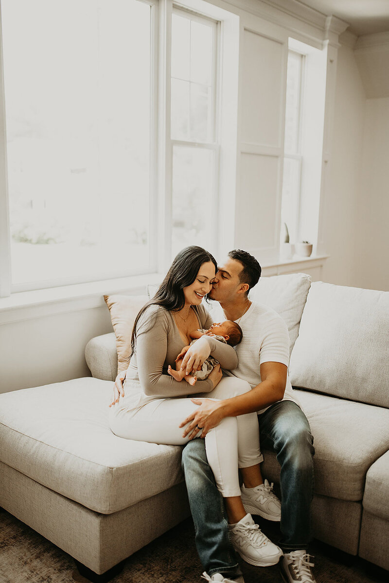 Young parents sitting on the couch, tenderly holding their newborn in the warmth of their home.