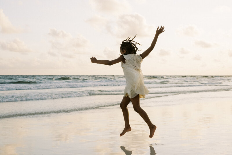 A little girl jumping over the waves in her white dress in Rosemary Beach, Florida.