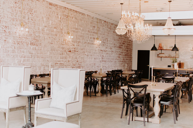 Interior of our event space showcasing our exposed brick wall, lounge chairs, tables, wooden chairs, and candles.