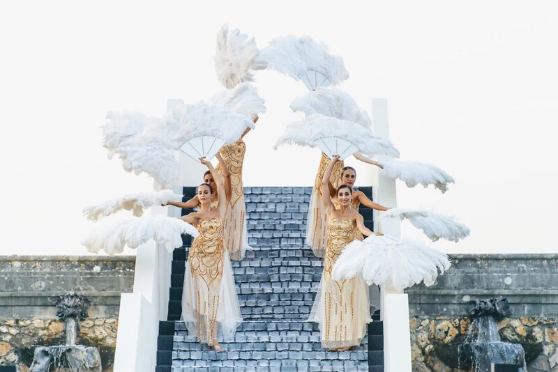 Women descending stairs holding white feather fans