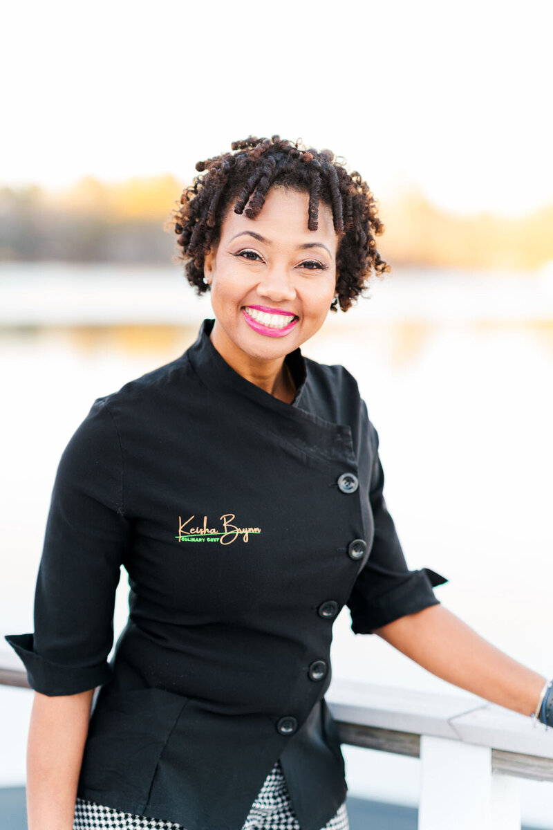 Woman standing on a dock in a black chef coat smiling at the camera