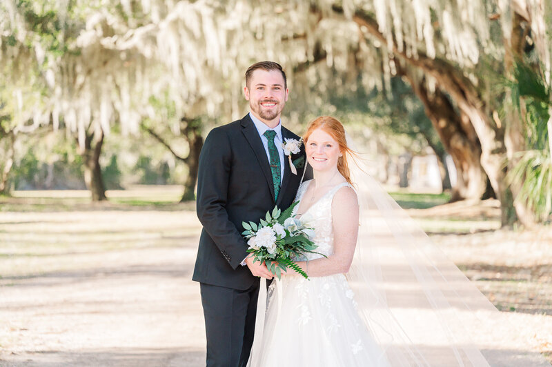 A bride and groom smiling under Spanish moss trees in Beaufort enjoying their North Carolina wedding photography