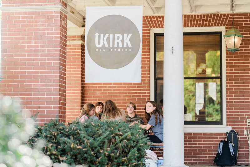 old historic brick home with white pillar and UKIRK banner with students sitting on front porch