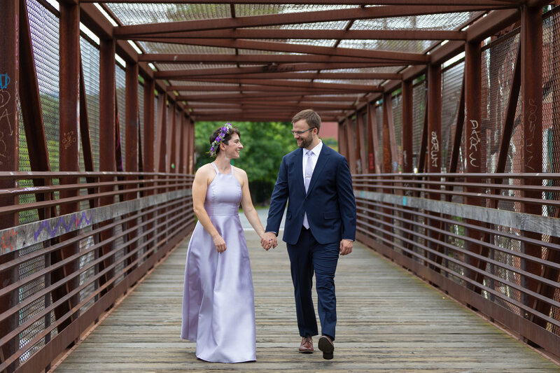 A couple holding hands and walking across a bridge.