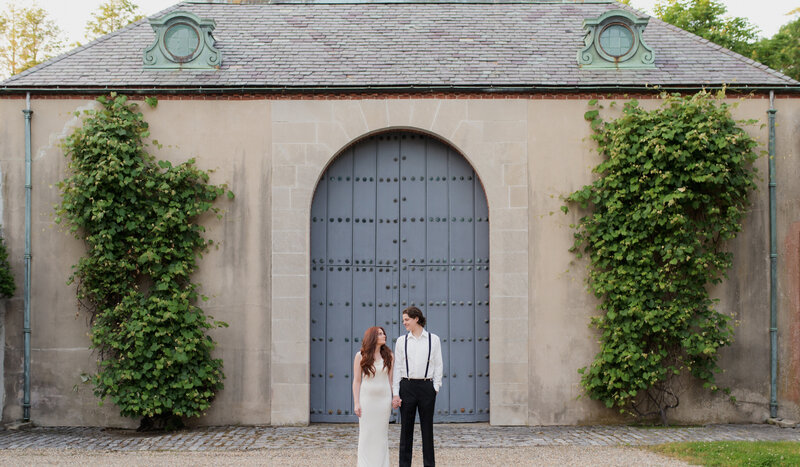 engagement session at a country side estate with couple standing in front of large carriage house door.
