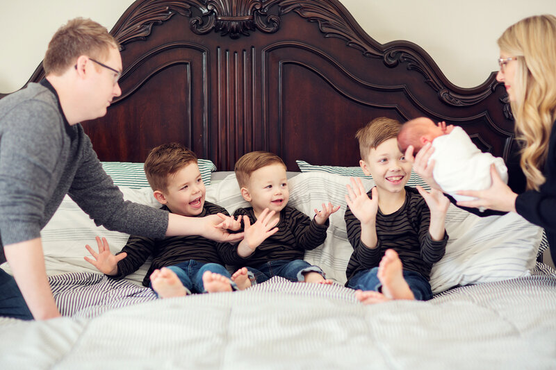 Brothers on a bed excitedly waiting to hold their new baby brother while mom and dad help.