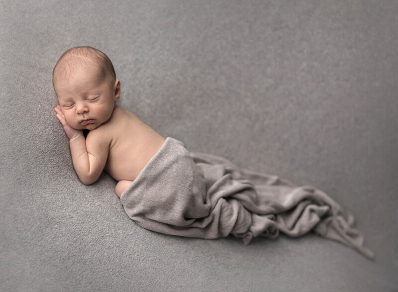 Sleepy baby boy in gray at his newborn photoshoot