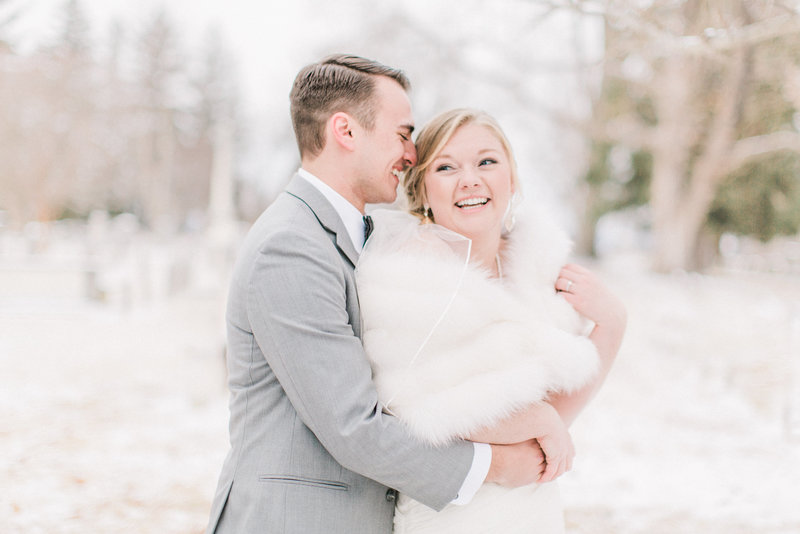 groom embraces his bride wearing white fur on their cold snowy wedding day