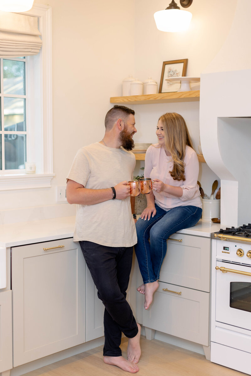 man and woman smiling at each other while clinking their coffee mugs toghether