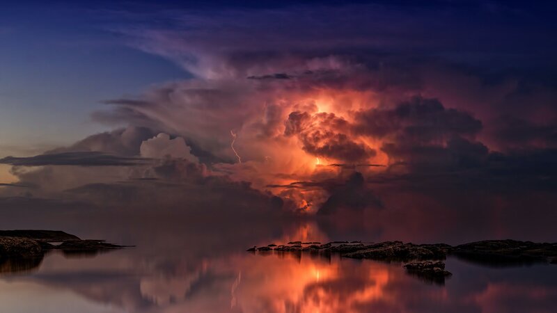 lightning bolts in large clouds above water