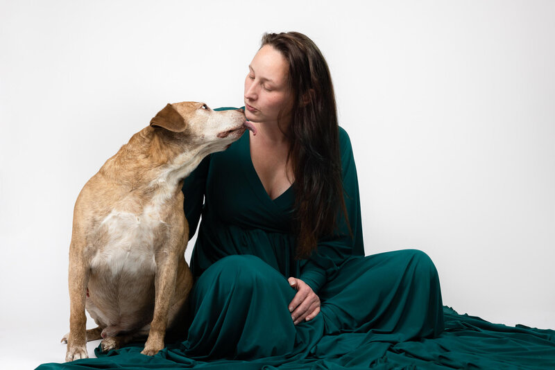 Female Veteran and LGBT photographer wearing a green long sleeved gown recievign a kiss from her tan and white brindle rescue mutt dog