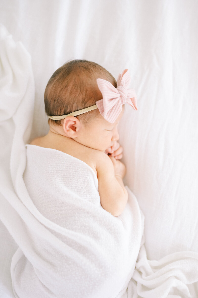 newborn baby with a pink bow laying on a bed
