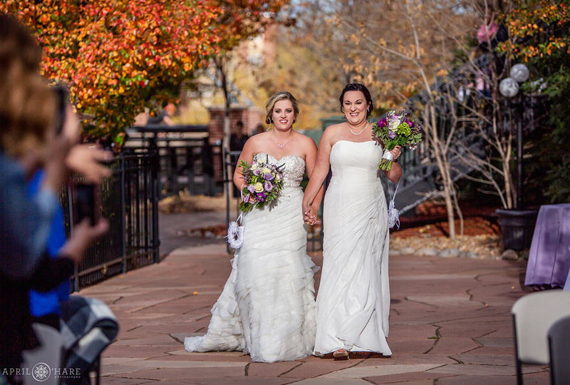 Two Brides walk into their courtyard wedding ceremony at the Golden Hotel during fall