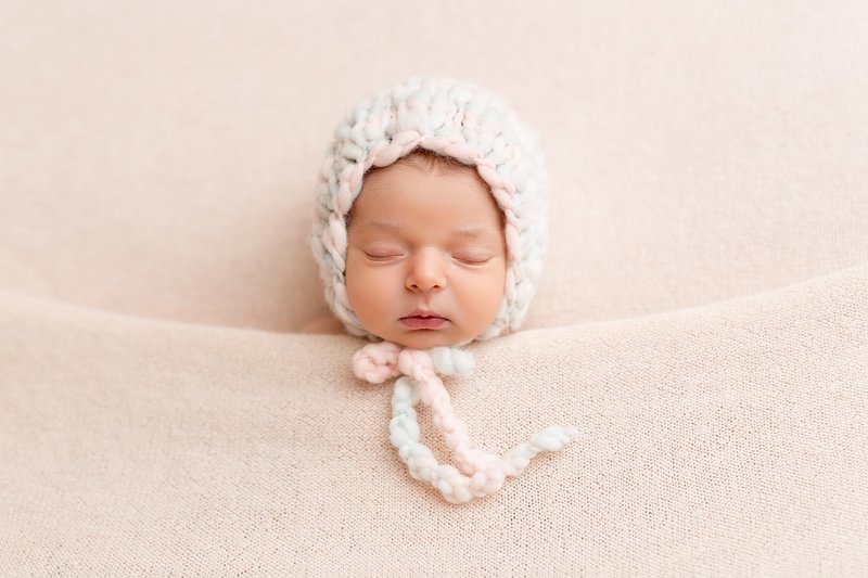 Newborn photography tucked in pink bonnet