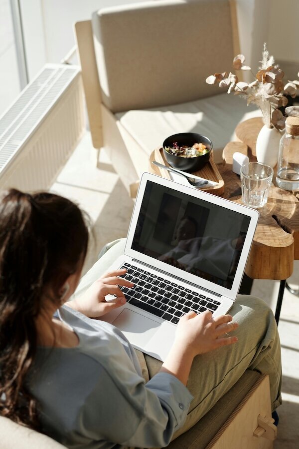 Person on laptop in a bright, cozy room with coffee and breakfast bowl, representing virtual non diet nutrition counseling.