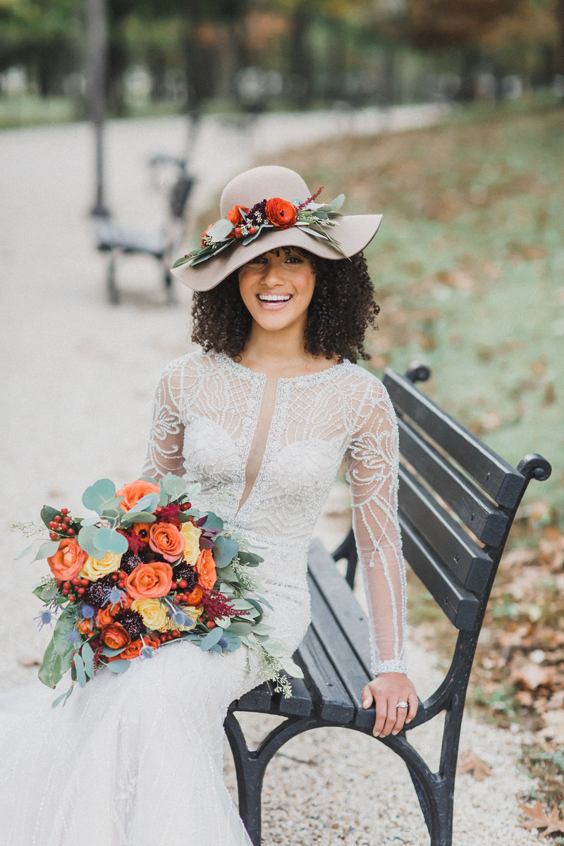bride with autumn flowers orange red blue yellow green on park bench