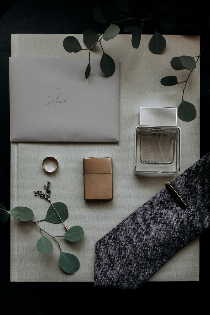 details for groom on their elopement day with gold lighter, cologne, vows, ring, and tie
