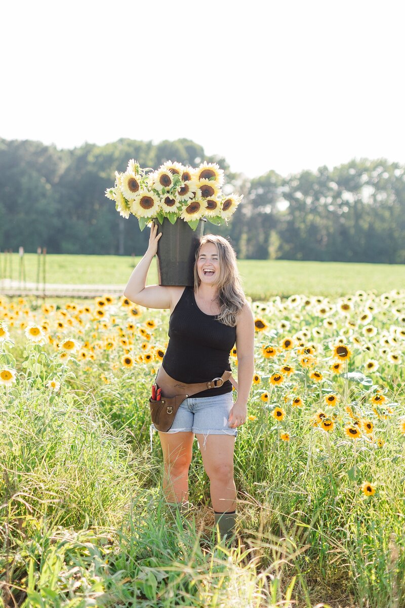 Woman standing in a field of sunflowers holding a bucket of flowers