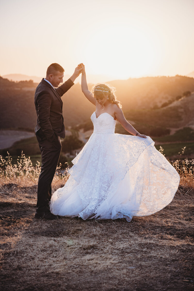 Groom spinning bride in front of a beautiful sunset