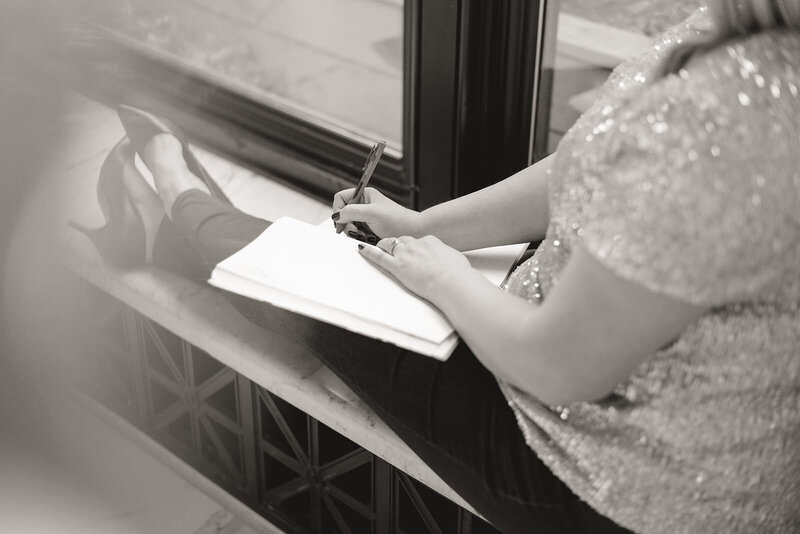 Women in sparkly blouse writes in a notebook by the window