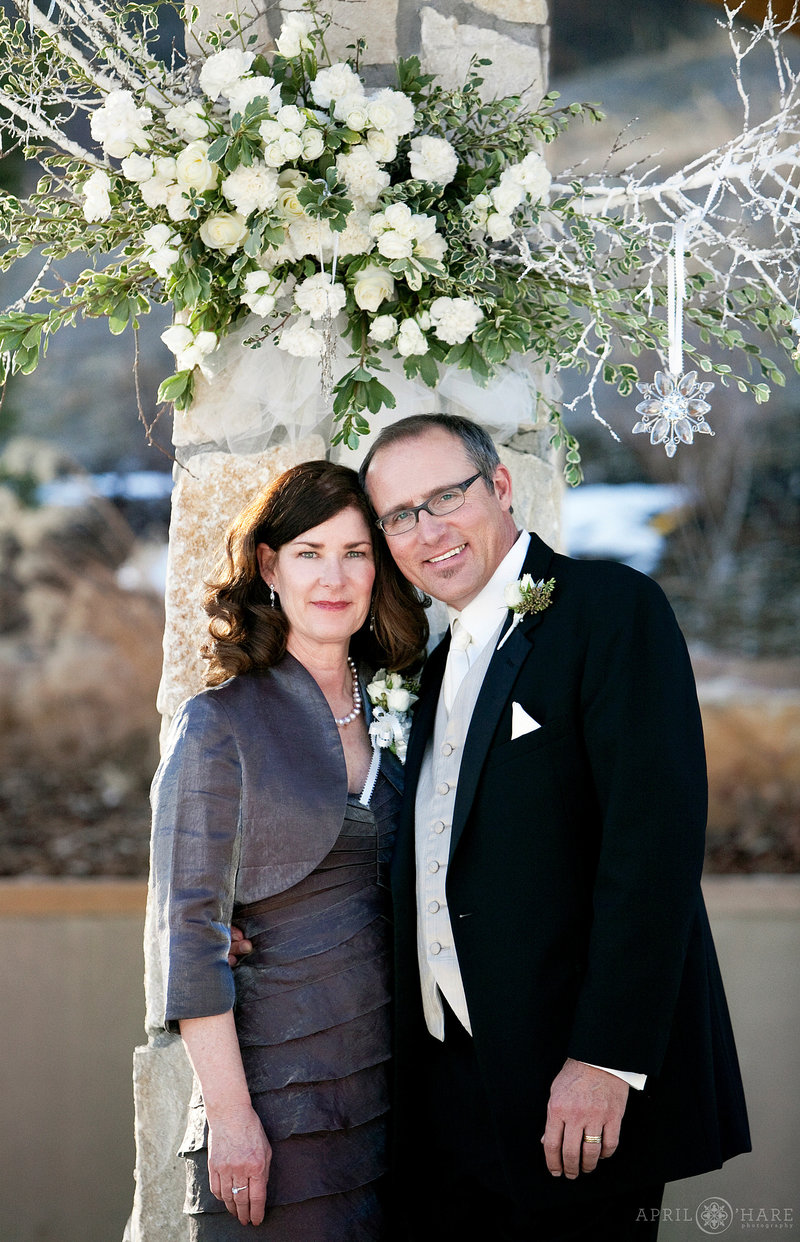 Parents of the bride get a portrait with the beautiful winter florals with glass snowflakes at a wedding at Cielo in Castle Pines