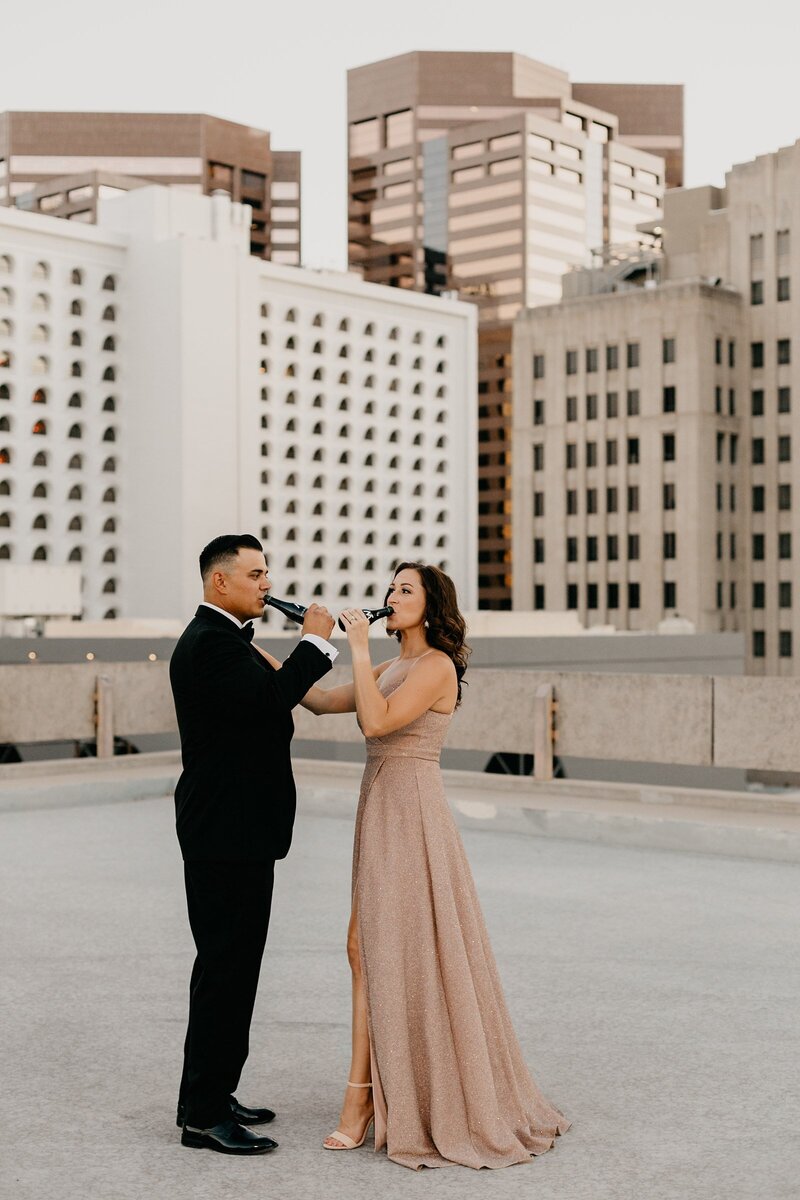 Engagement photo of couple drinking champagne on top of a parking garage in downtown Phoenix AZ