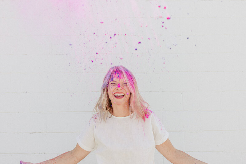 Joyful image of a busy mom tossing chalk powder into the air, smiling radiantly against a white backdrop