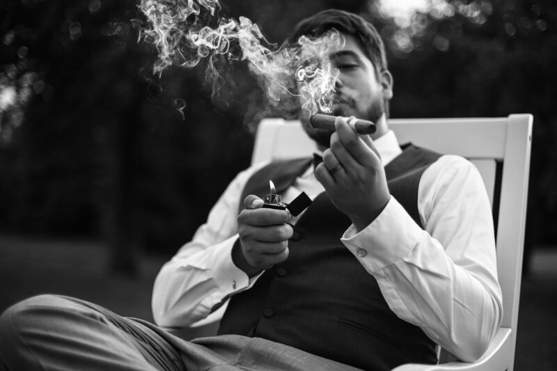 Groom smokes a cigar during wedding reception  at Whispering Trees Manor