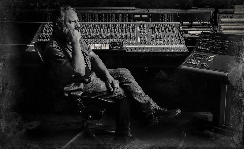 musician portrait Dan Joeright sitting sideways at recording console in black and white