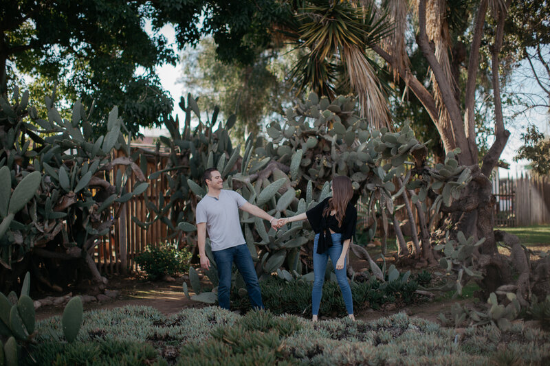Couple holding hands standing in front of cactus during San Diego portrait session