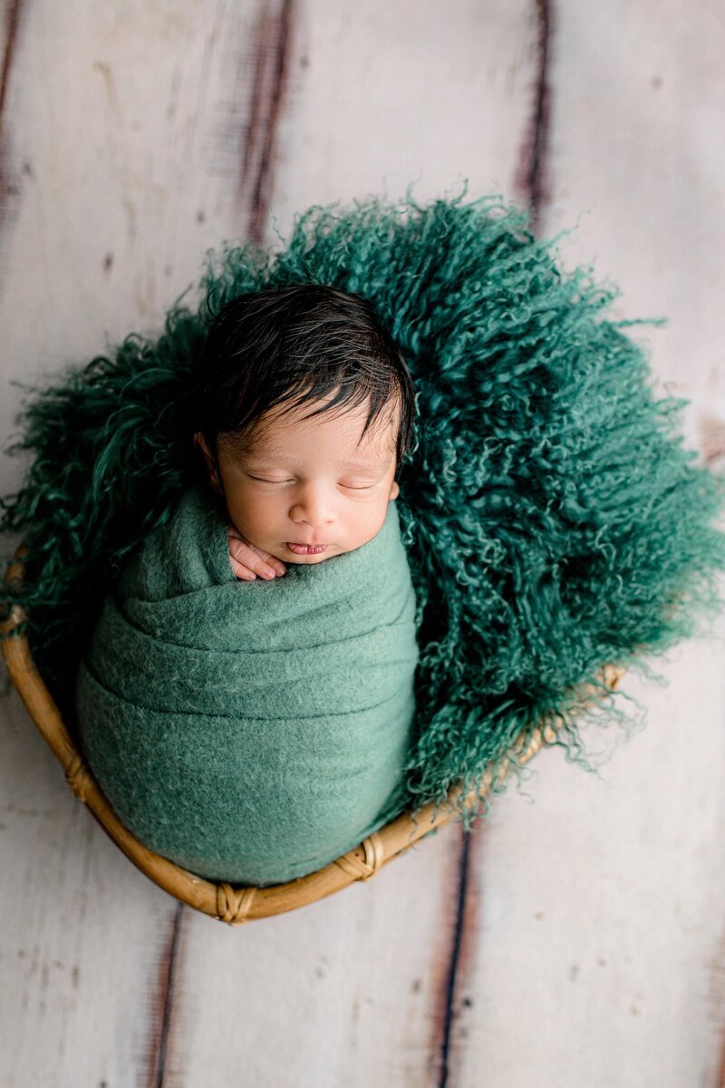 Newborn boy is wrapped in a teal layer in a basket during his Studio newborn session