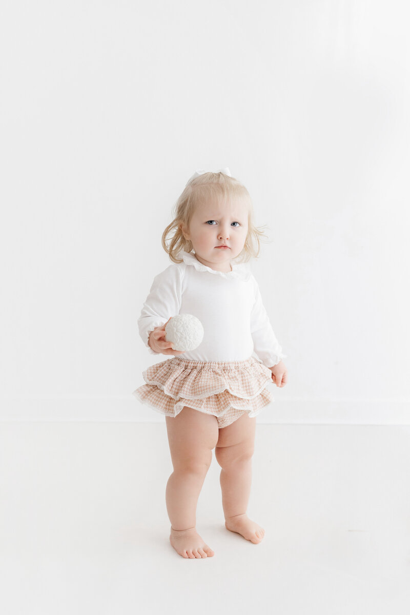 Frowning one year old baby girl looking into the camera on her photoshoot in Cheshire