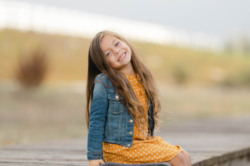 little girl smiling sitting on a wood sidewalk