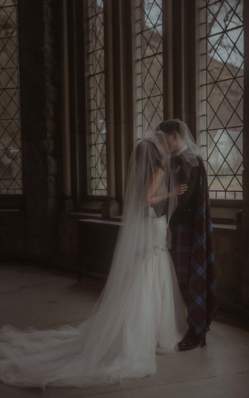 Couple sharing a kiss under the veil in St. Kirk, Scotland, captured in a timeless, romantic moment, surrounded by the church's beauty and historic charm