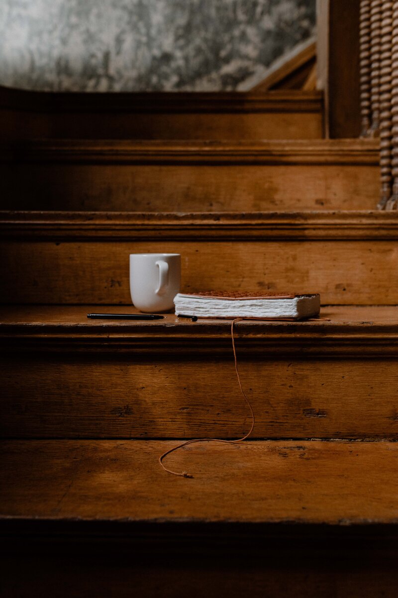White mug, black pen, and notebook filled with notes from a website copy audit on a wood staircase