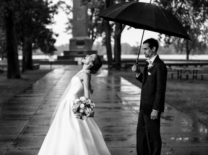 Bride stands in the rain while groom holds umbrella at Presque Isle State Park