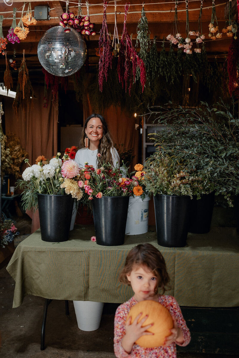 Florist Sara Davies pictured with flowers  in her studio and a disco ball is hanging from the ceiling amongst dried flowers.