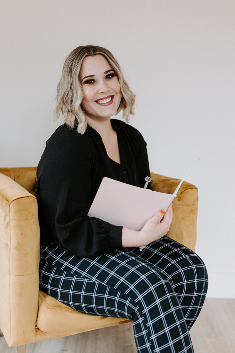 person sitting in a chair smiling while holding a notebook