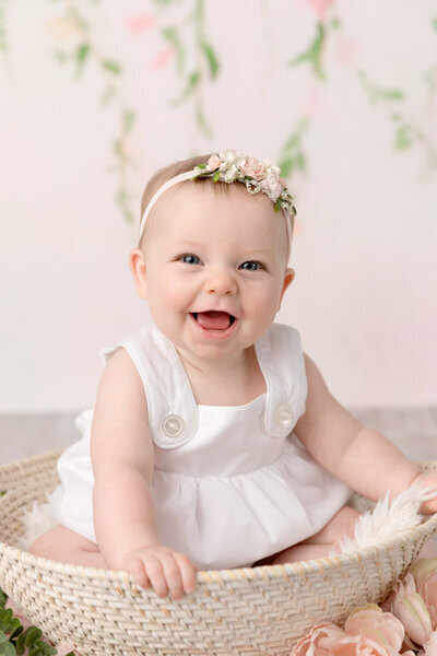baby girl smiles against a light pink floral background