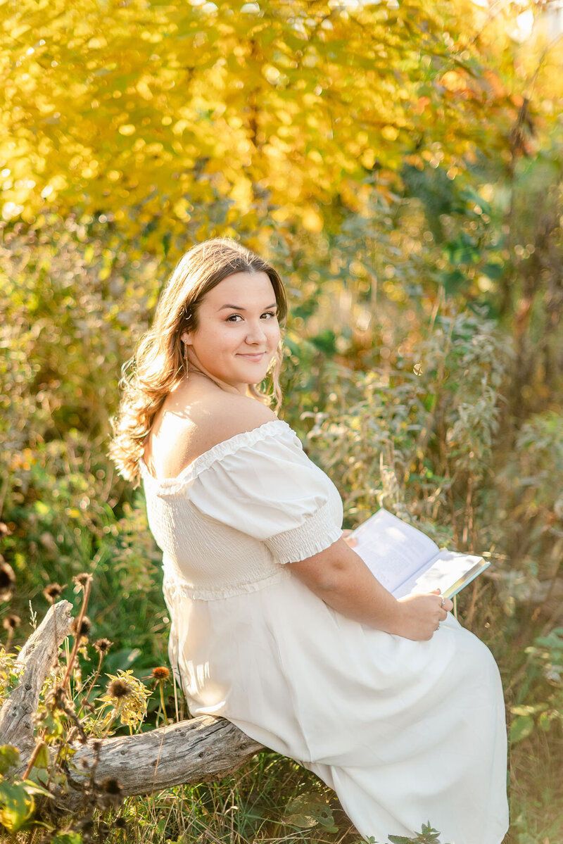 High school senior girl in white dress holding a book and looking back at the camera by Chicago graduation photographer Kristen Hazelton