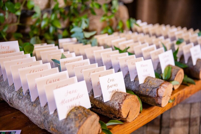 Calligraphy escort cards displayed in a wood stand for a rustic wedding