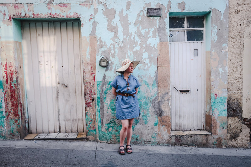 Michelle-Marie Gilkeson in blue dress and large hat stands on a sidewalk in Mexico