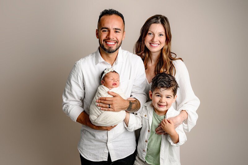 father holds his newborn baby daughter while his wife and son stand beside him