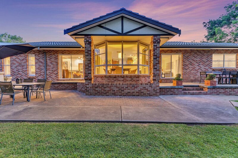 Sunset exterior photo of a brick family home featuring a bay window, outdoor entertaining space, and tidy front patio.