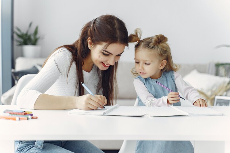 mother helping preschooler with homeschool writing at table