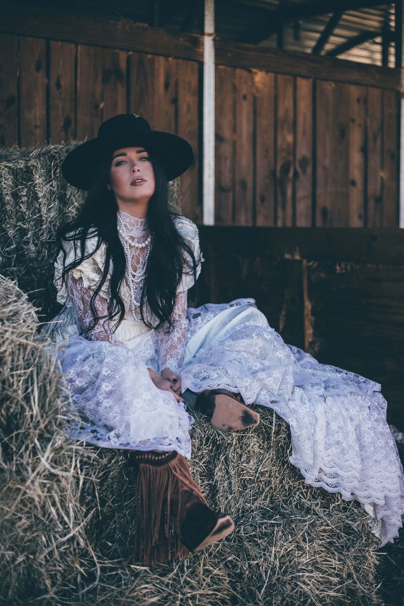A woman in a white dress sitting on hay bales captured by elopement photography expert Britt Elizabeth